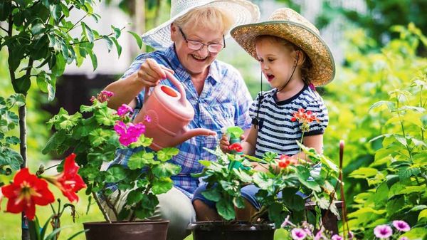 Eine ältere Dame gießt Blumen mit einem jungen Mädchen in einem bunten Garten.