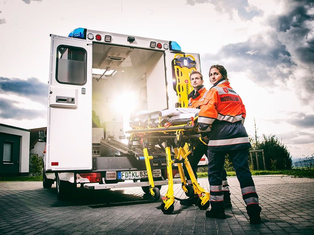 Malteser Rettungsdienstmitarbeiter tragen eine Rettungswagen Liege.