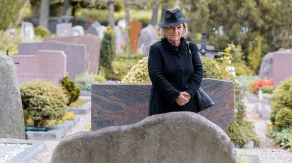 Eine schwarz gekleidete Frau, die einen Friedhof besucht.