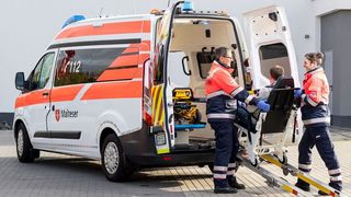 Zwei Malteser Mitarbeiter helfen einem gehbehinderten Menschen ins Fahrzeug.