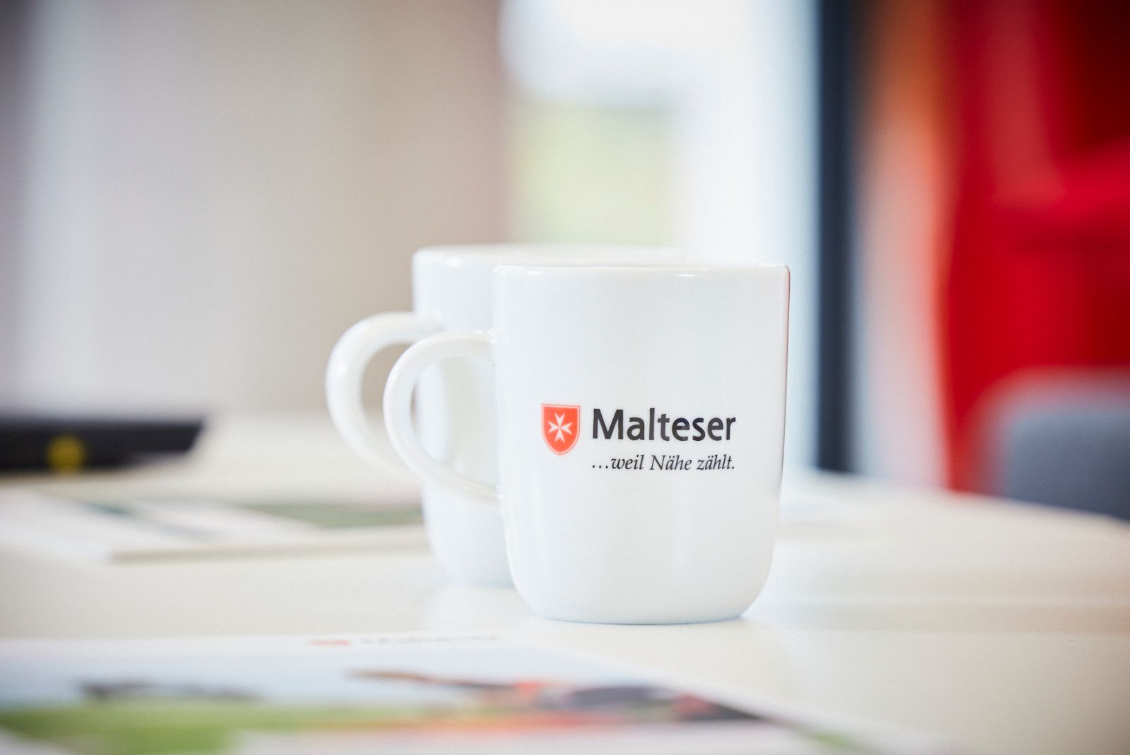 Weisse Malteser Tasse bedruckt mit Malteser Logo und Malteser–weil–Nähe–zählt-Schriftzug.