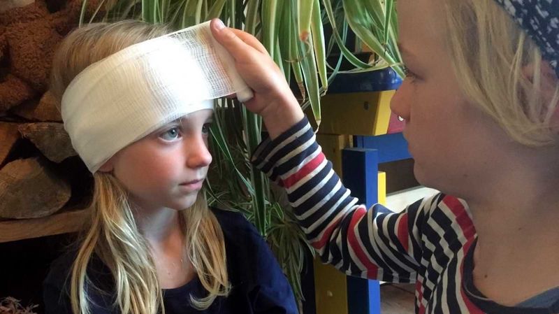 Ein kleines Mädchen verbindet einem anderen Mädchen den Kopf.