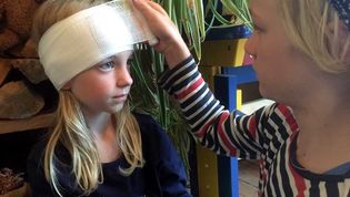 Ein kleines Mädchen verbindet einem anderen Mädchen den Kopf.