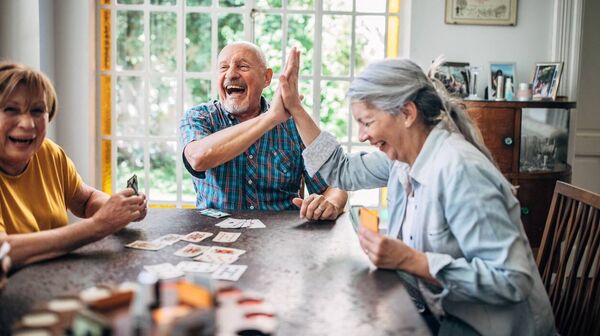 Eine Gruppe älterer Menschen spielt gemeinsam Karten, lacht dabei und klatscht sich gegenseitig in die Hände.