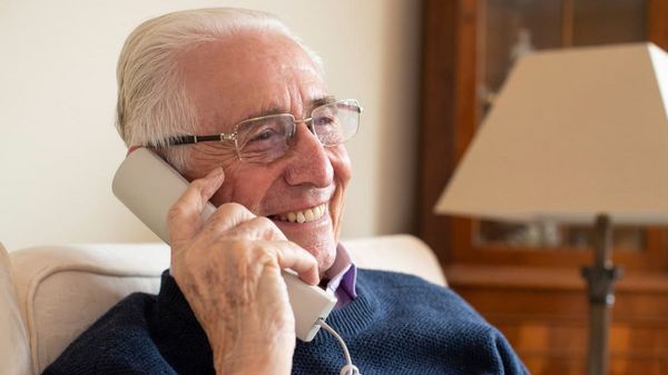 Lächelnder alter Mann mit Telefonhörer am Ohr.