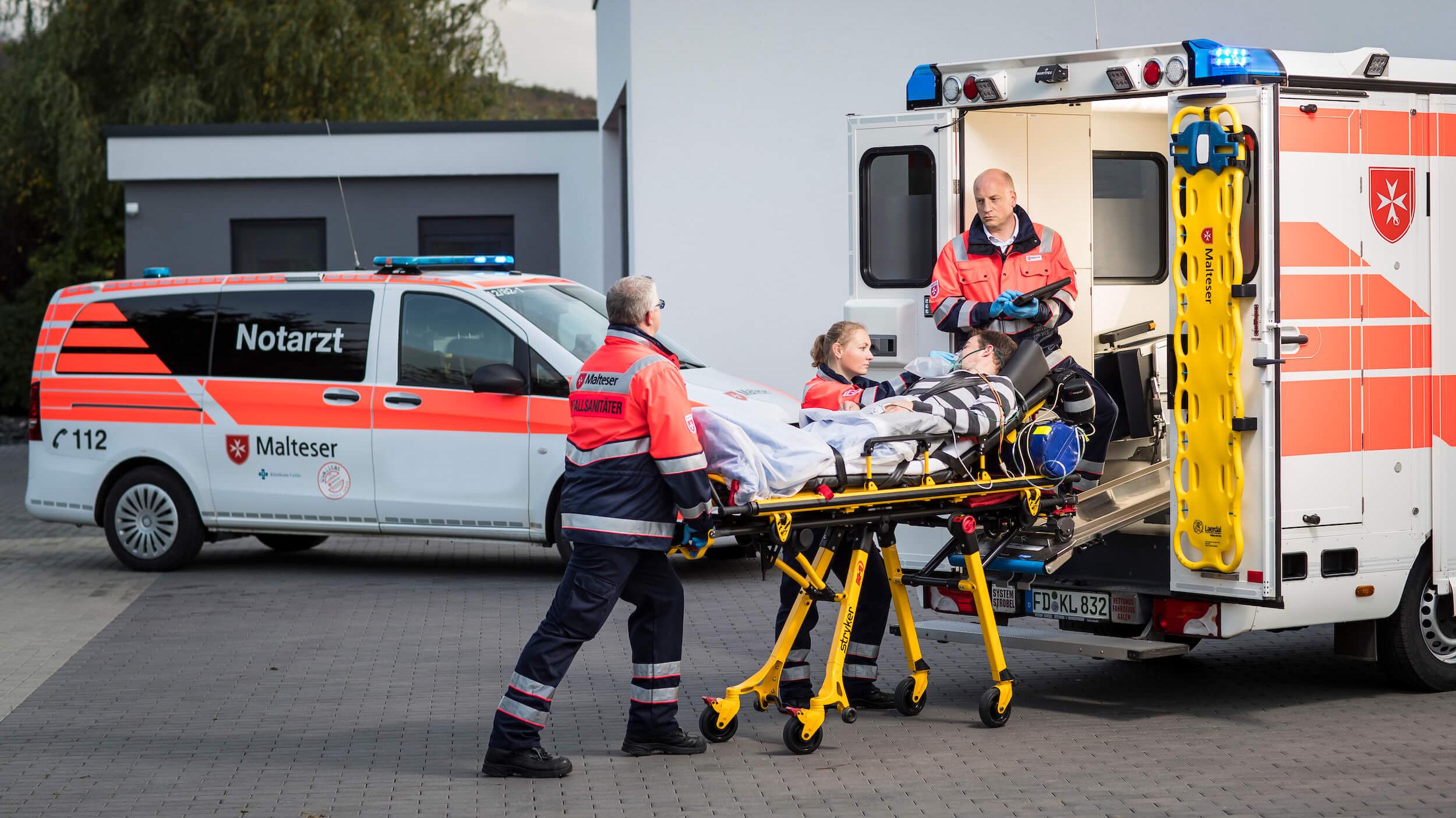 Drei Rettungsdienstsanitäter schieben Trage mit Patienten in den Rettungswagen