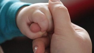 Eine Kinderhand umschließt den Finger einer erwachsenen Person.