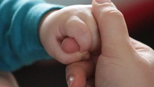 Eine Kinderhand umschließt den Finger einer erwachsenen Person.