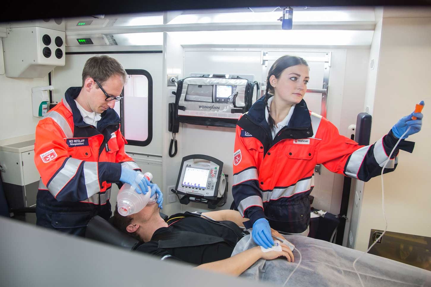 Notfallsanitäter der Malteser helfen einem Mann im Rettungswagen.