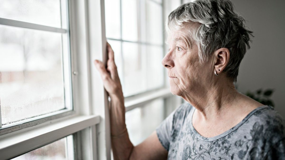 Eine ältere Frau schaut traurig aus dem Fenster.