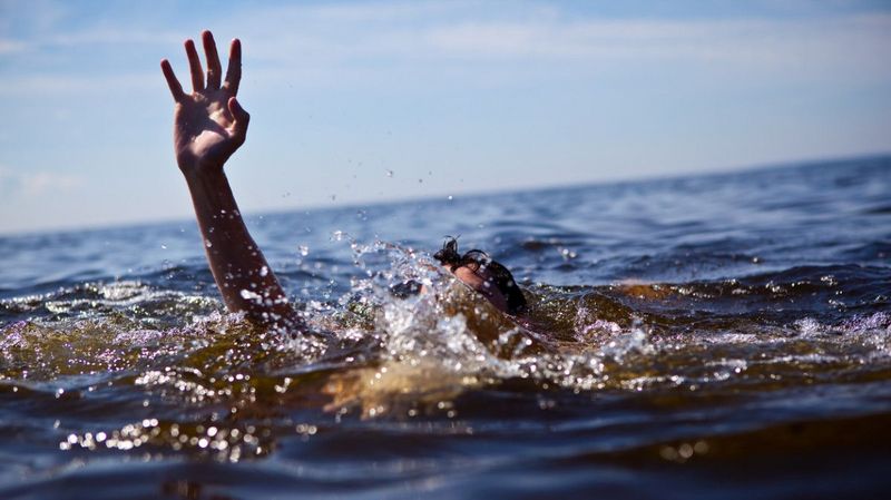 Person ertrinkt im Wasser und reckt den Arm in die Luft