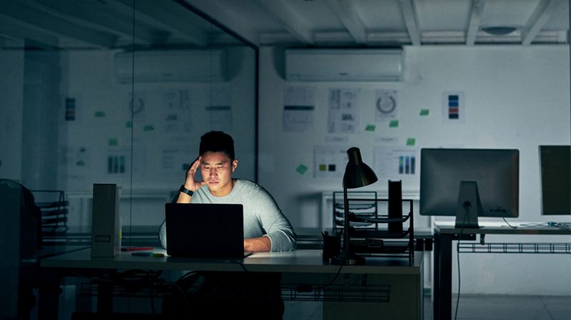 Junger asiatischer Mann in einem dunklen Büro vor einem Bildschirm