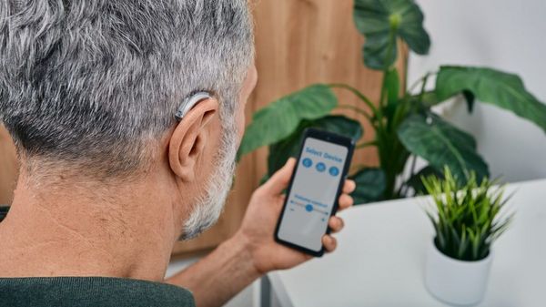 Mann mit Hörgerät schaut auf ein Smartphone