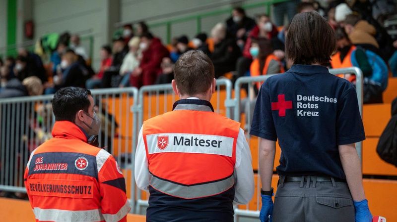 Drei Menschen mit Kleidung deutscher Hilfsorganisationen stehen mit dem Rücken zur Kamera