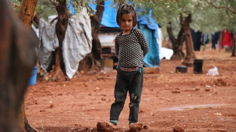 Ein junges Mädchen unter Bäumen in einem Flüchtlingscamp.