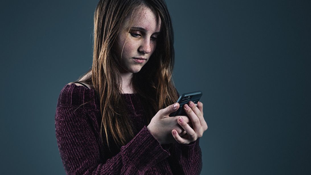 Junges Mädchen schaut mit resigniertem Gesichtsausdruck auf ein Smartphone