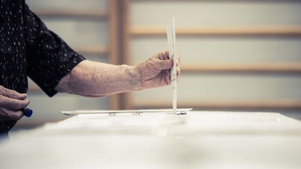 Es wird ein Stimmzettel gezeigt, welcher in eine Wahlurne geworfen wird.