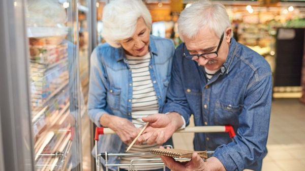 Ein älteres Paar mit Einkaufswagen und Einkaufsliste in einem Supermarkt.