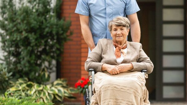Eine ältere Frau im Rollstuhl wird von einem Mann geschoben.