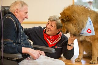 Senior im Rollstuhl und Malteser Helferin mit ihrem Hund