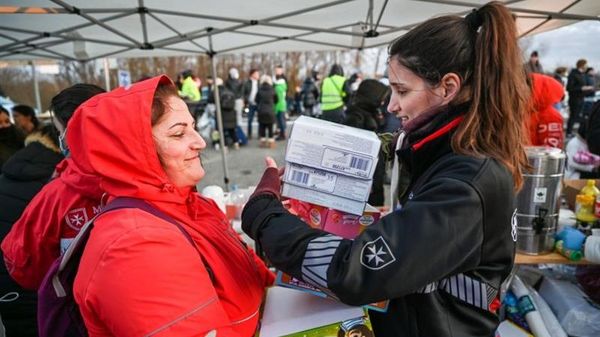Eine Junge Frau übergibt Kartons mit Lebensmitteln an eine lächelnde Frau in einer roten Jacke