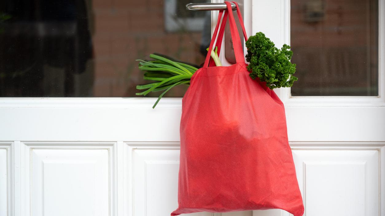 Eine Einkaufstasche mit Lebensmitteln hängt an einer Türklinke.
