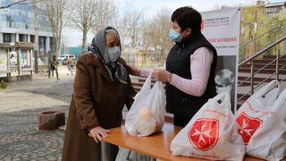 Malteser Mitarbeiterin verteilt Taschen mit Lebensmitteln an eine bedürftige ältere Frau in der Ukraine. 