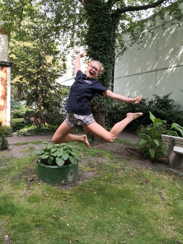 Jana springt im Garten hoch und lacht.