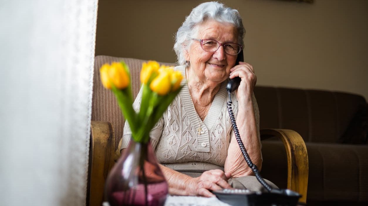 Eine alte Frau telefoniert in einem Wohnzimmer.