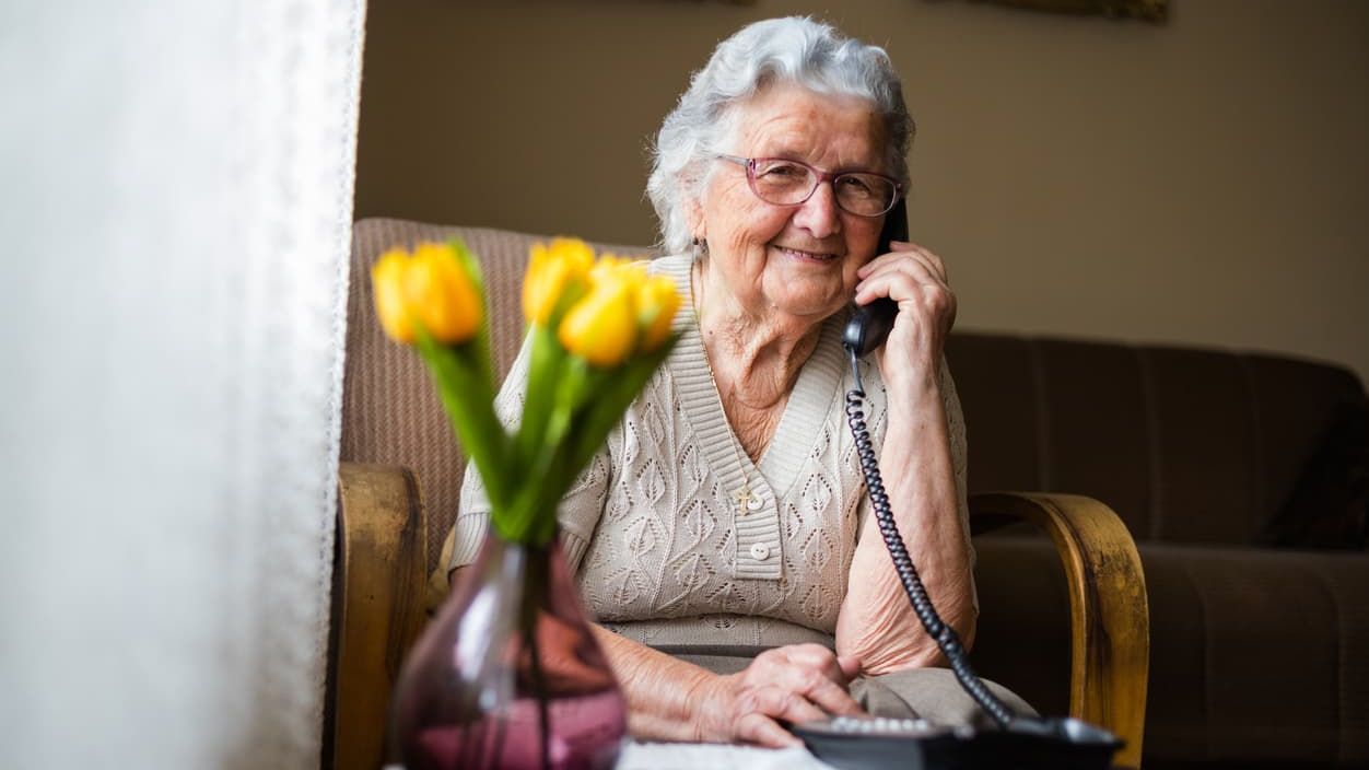 Eine alte Frau telefoniert in einem Wohnzimmer.