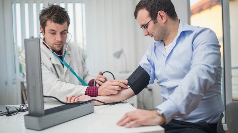 Ein junger Arzt misst Blutdruck bei einem Mann mit Brille