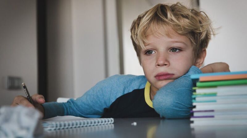 Ein Junge mit müdem Gesicht macht Hausaufgaben