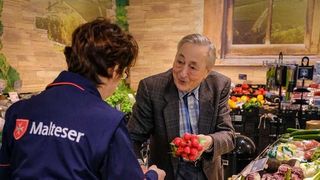 Malteser Helferin unterstützt einen älteren Mann beim Einkaufen im Supermarkt.