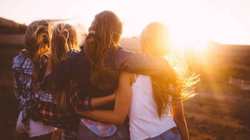 Vier Mädchen haben sich in den Armen und schauen in den Sonnenuntergang.