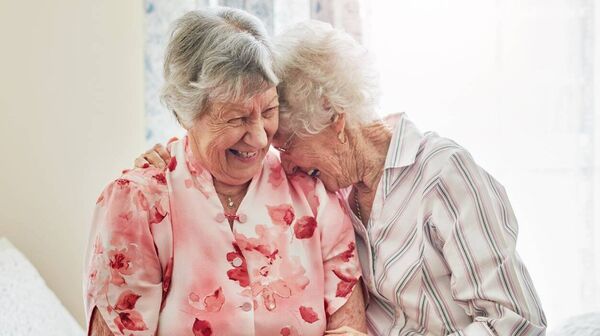 Zwei ältere Damen lachen herzlich und liegen sich dabei in den Armen.