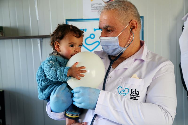 Ein Arzt mit einem Kleinkind und einem Luftballon auf dem Arm.