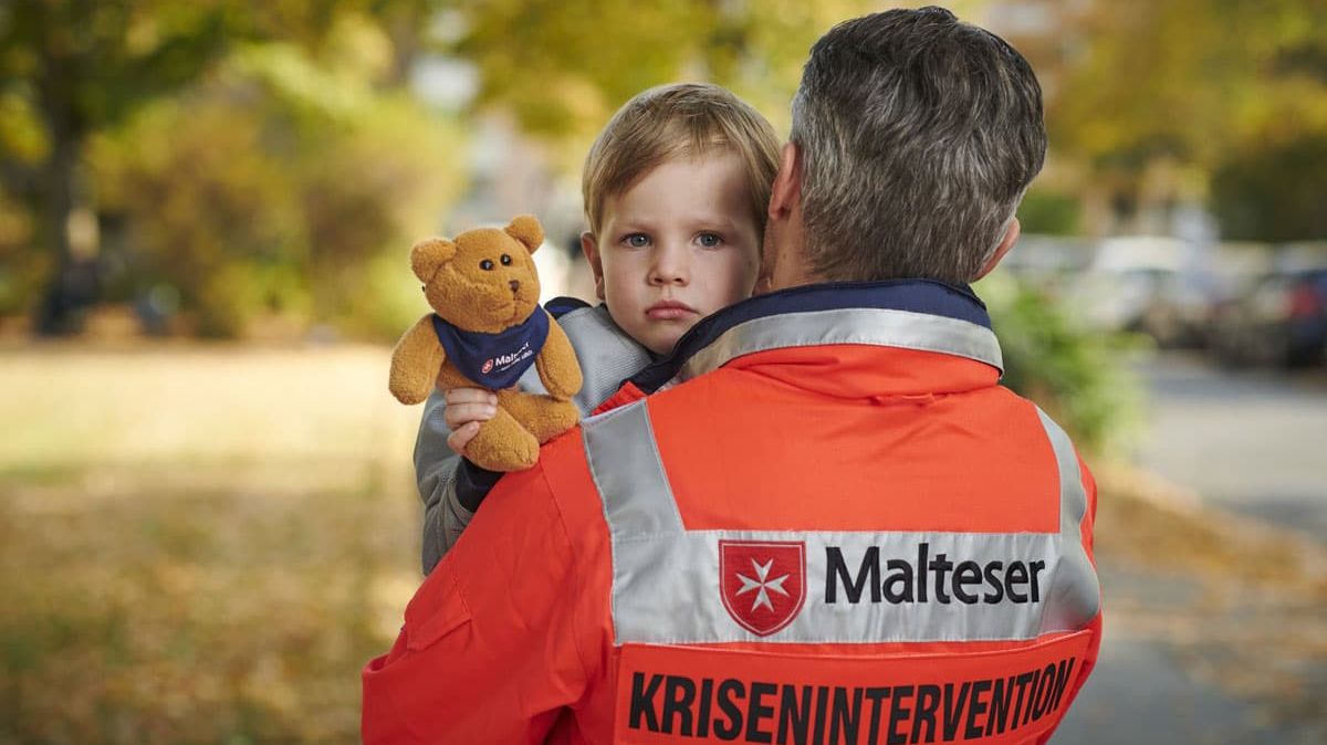 Ein Mitarbeiter der Malteser Psychosozialen Notfallversorgung trägt ein junges Kind auf dem Arm.