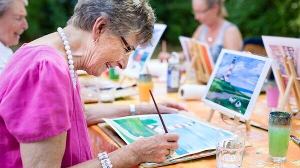 Ältere Frauen malen Bilder von einem Leuchtturm.