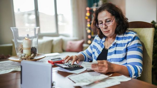 Frau mit Brille sitzt mit einem Taschenrechner an einem Tisch mit Rechnungen.