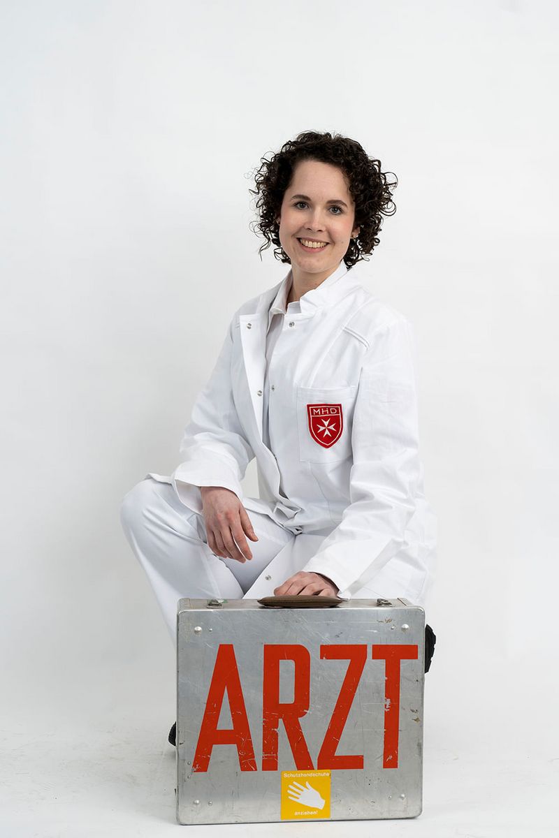 Eine Frau in einem Arztkittel mit einem Koffer, auf dem groß das Wort „Arzt“ steht
