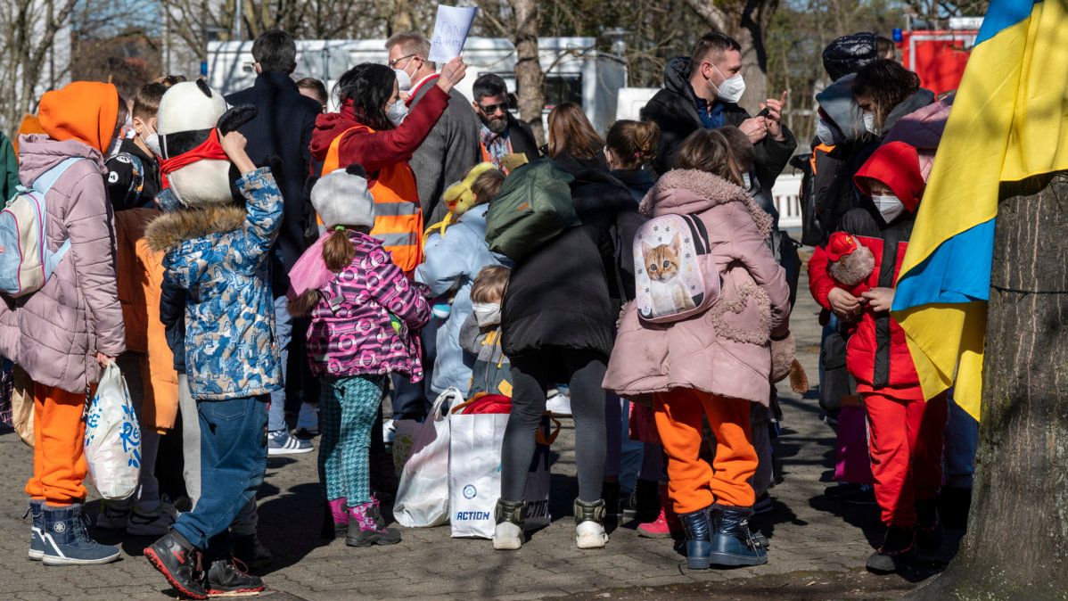 Geflüchtete ukrainische Kinder; auf der rechten Seite eine ukrainische Flagge an einem Baum.
