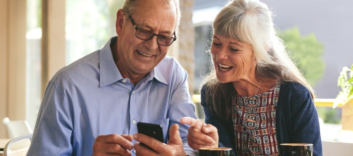 Ein älteres Paar sitzt in einem Café mit Smartphone.