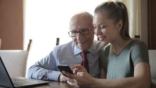Eine jüngere Frau erklärt einem älteren Mann Smartphone und Tablett