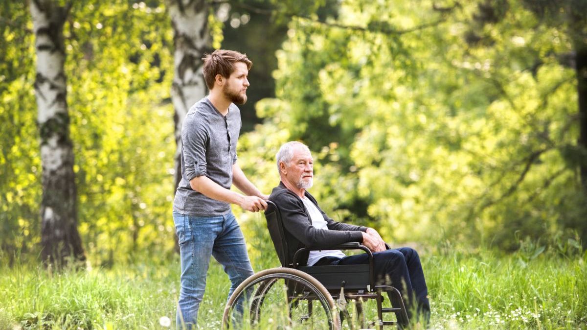 Ein junger Mann schiebt einen älteren Mann im Rollstuhl