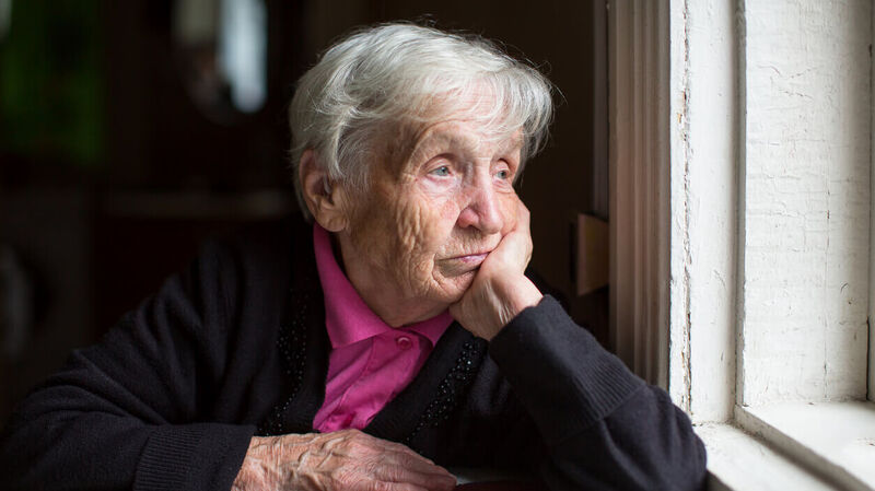 Eine ältere Frau schaut traurig aus einem Fenster