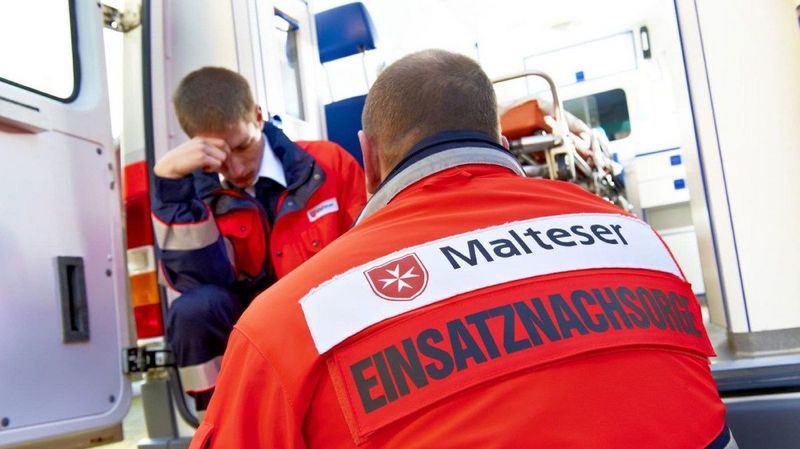 Zwei Männer in Einsatzkleidung der Malteser am Heck eines Rettungswagens