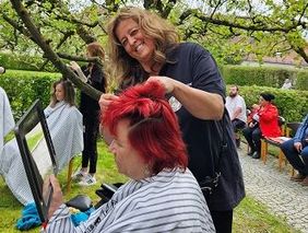 Eine Frau schneidet einer anderen Frau in einem Garten die Haare.