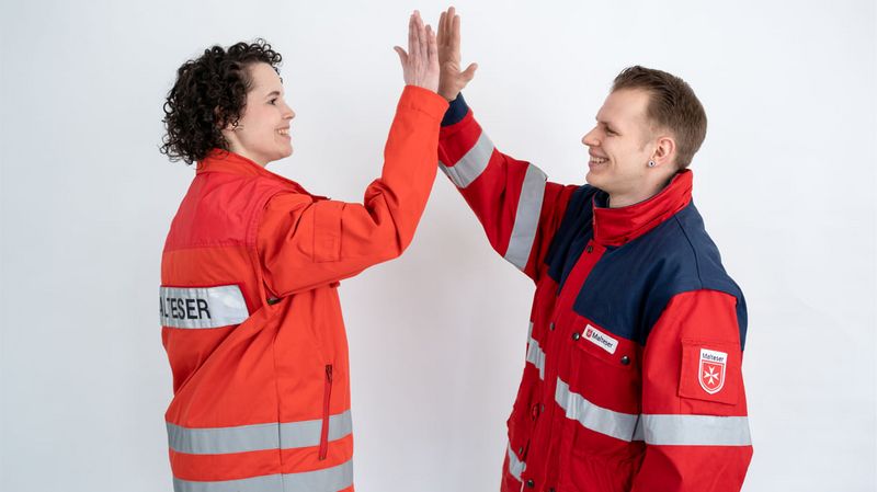 Eine Frau und ein Mann mit Einsatzjacken des Malteser Hilfsdienstes geben sich ein „High Five“