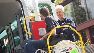 Malteser Mitarbeiter hilft Mann im Rollstuhl in den Transporter