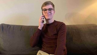Junger Mann mit Brille sitzt auf einem Sofa und telefoniert
